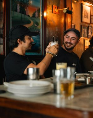 Two friends enjoy drinks and laughter in a cozy London pub, embodying camaraderie and warmth.